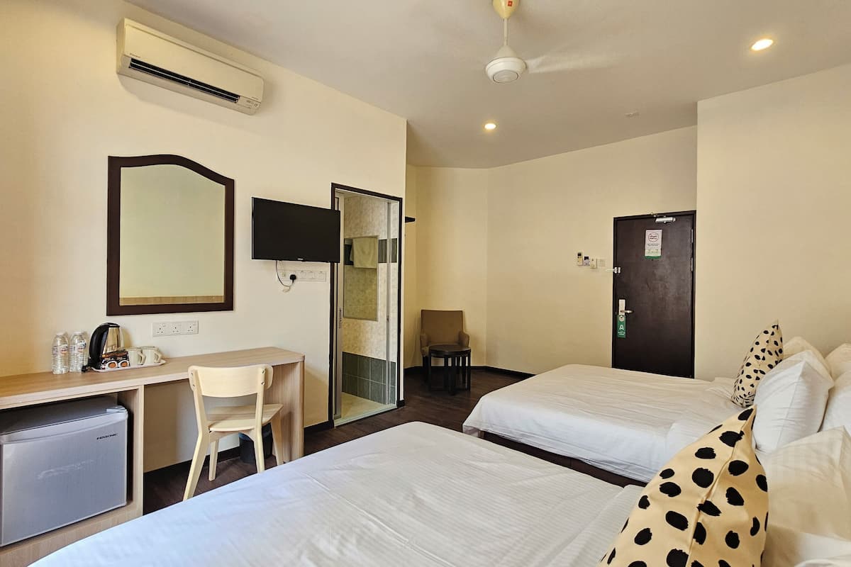 A hotel room with two beds, a desk with a chair, a small table, a mirror, an air conditioning unit, and a ceiling fan.