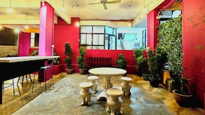 A cozy indoor space with a round table surrounded by stools, potted plants, and a red wall. - HOTEL 22 GURNEY (George Town)