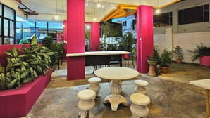 A spacious indoor area with a round table and stools, surrounded by potted plants and a red pillar. - HOTEL 22 GURNEY (George Town)