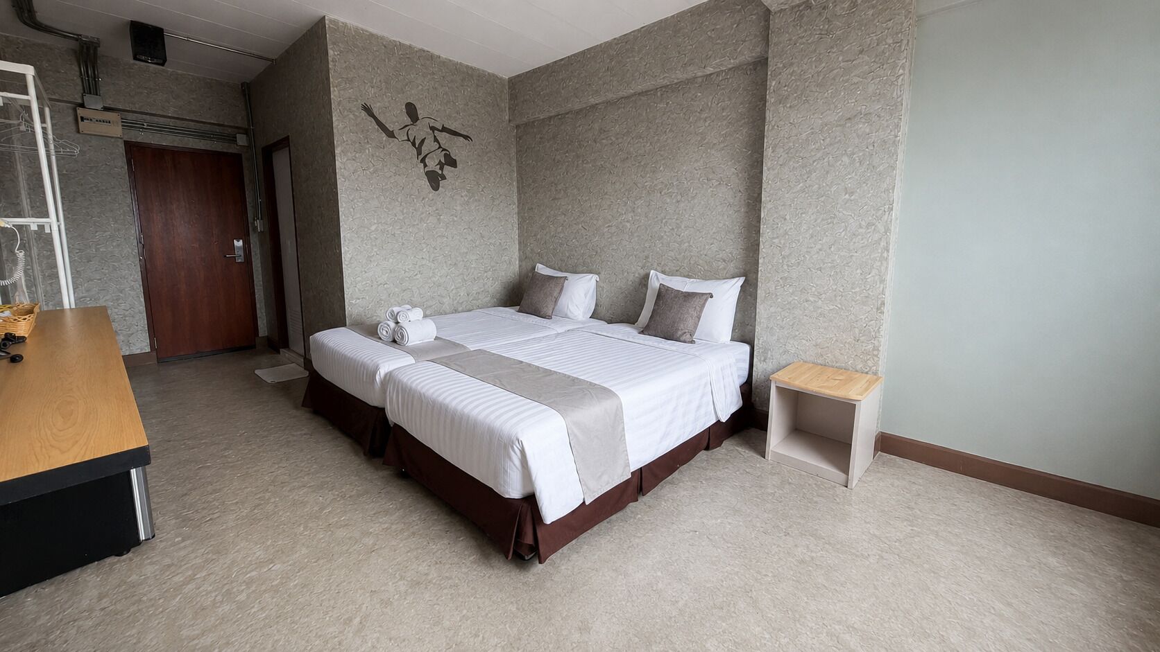 A hotel room with a double bed, a wooden desk, and a small bedside table.