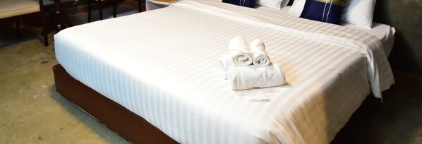 A neatly made bed with a striped bedspread and two rolled towels on the side.