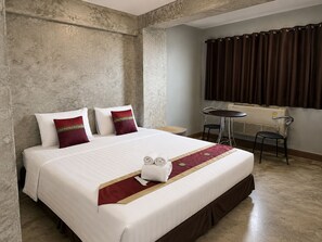 A hotel room with a large bed, two pillows, a small table with chairs, a window with curtains, and a radiator. - Happyland Mansion (Bangkok)