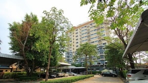 A parking area with several cars, surrounded by trees and a multi-story building in the background. - Happyland Mansion (Bangkok)