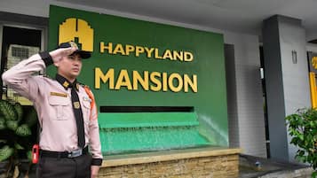 A security guard saluting in front of a building with a sign that reads "HAPPYLAND MANSION".