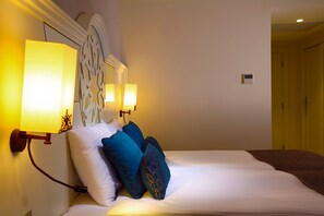 A neatly made bed with white and blue pillows, a decorative wall headboard, and two wall-mounted lamps.