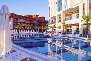 A swimming pool with lounge chairs and umbrellas, surrounded by multi-story hotel buildings with balconies.