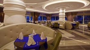 A spacious hotel dining area with multiple tables and chairs, large decorative columns, and a modern ceiling design. - Diamond Elite Hotel & Spa - Adults Only (Manavgat)