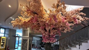 Un'ampia hall con un'esuberante composizione floreale artificiale al centro, una scalinata con ringhiere decorate e una chiara vista sulla zona ingresso.