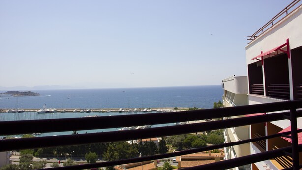 Vista sulla costa da un balcone, cielo sereno, un porto turistico con barche e un’isola in lontananza.