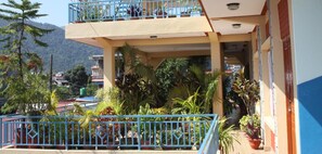 A building with a balcony, potted plants, and a mountainous background. - Nanohana Lodge (Pokhara)