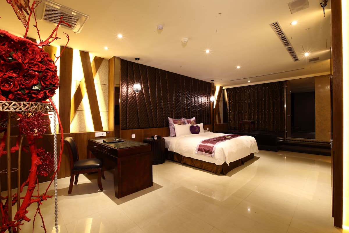 A hotel room with a large bed, a desk, and a chair. There is a decorative red tree on the left side of the room.