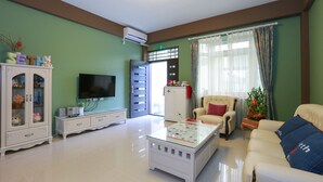 Una sala de estar con televisión, muebles blancos, una mesa de centro de vidrio y un sofá.