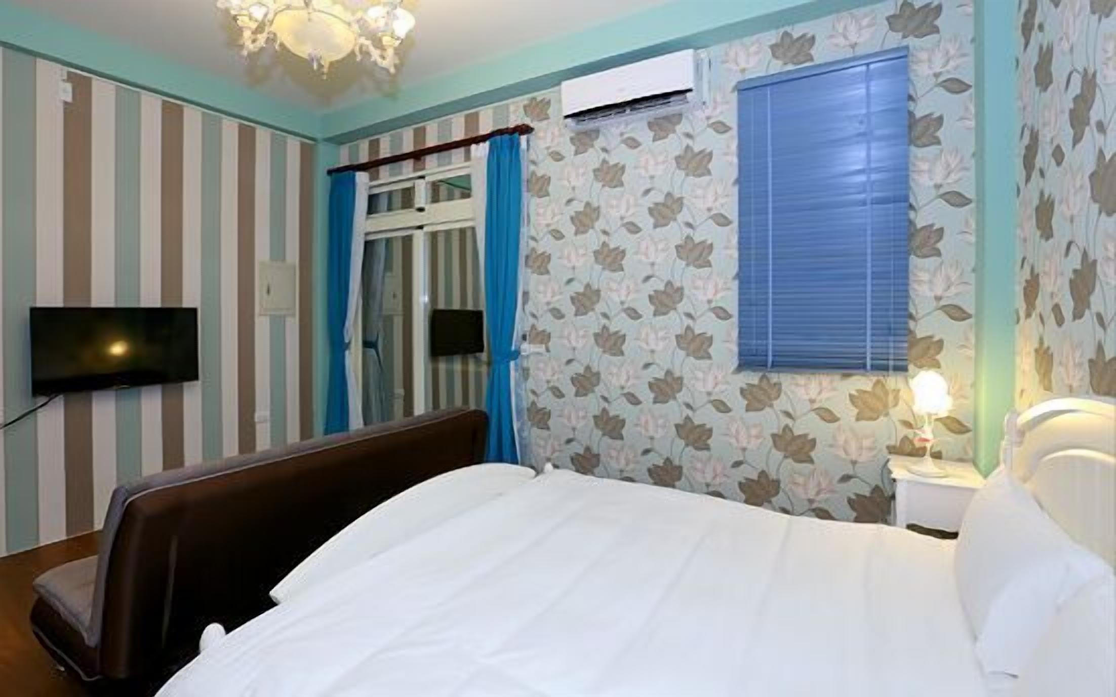 A bedroom with a bed, a TV, a window with curtains, and a wall-mounted air conditioner.