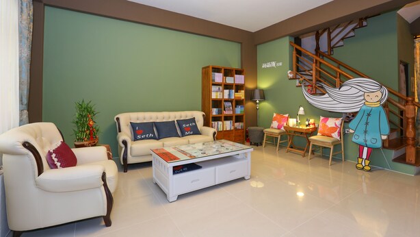 Una sala de estar con sofá, sillón, mesa de centro, estantería y una escalera.
