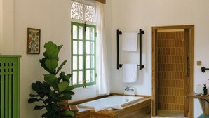 A bathroom with a bathtub, a wooden bench, a potted plant, and a green cabinet. - Baan Samsa (Luang Prabang)