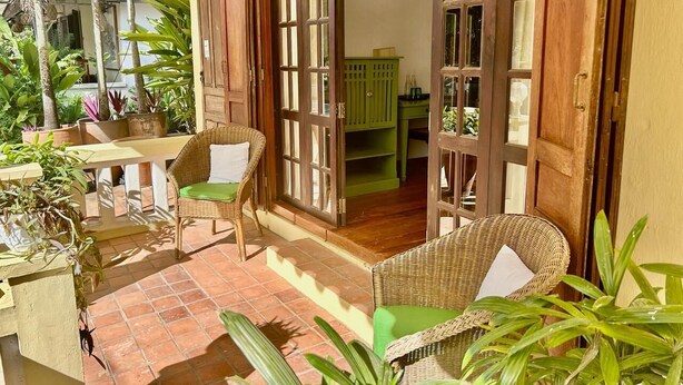 A patio with wicker furniture, a green cabinet, and potted plants. - Baan Samsa (Luang Prabang)