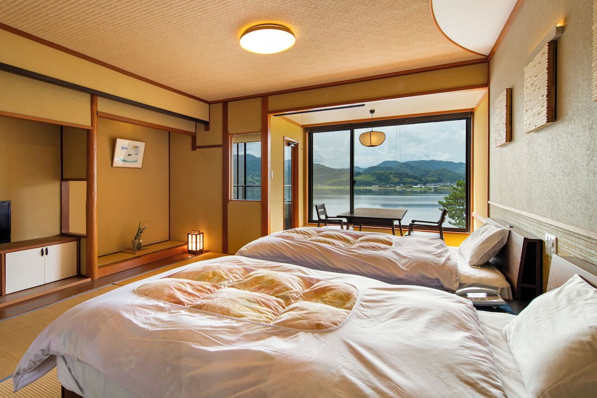 A hotel room with a bed, a TV, a desk, and a view of a lake.