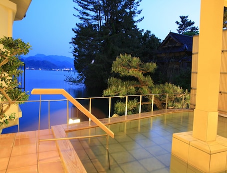 A terrace with a view of a lake and mountains, a wooden staircase, and a railing.