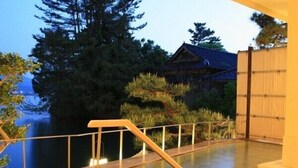 A serene outdoor area with a wooden deck, a bamboo fence, and a traditional building in the background. - Yunoyado Saika (Yurihama)