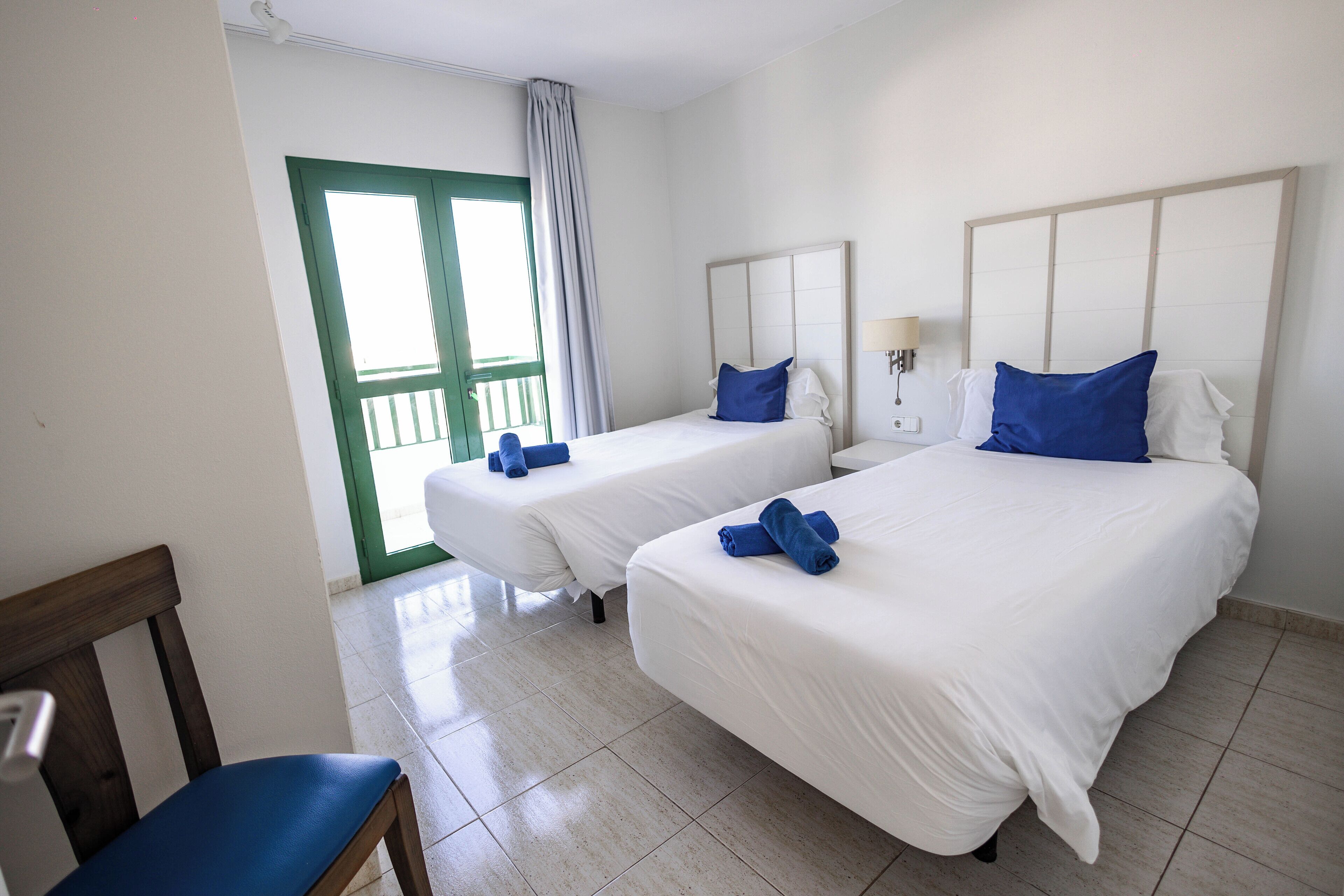 Habitación de hotel con dos camas, una silla y una puerta que da al exterior.