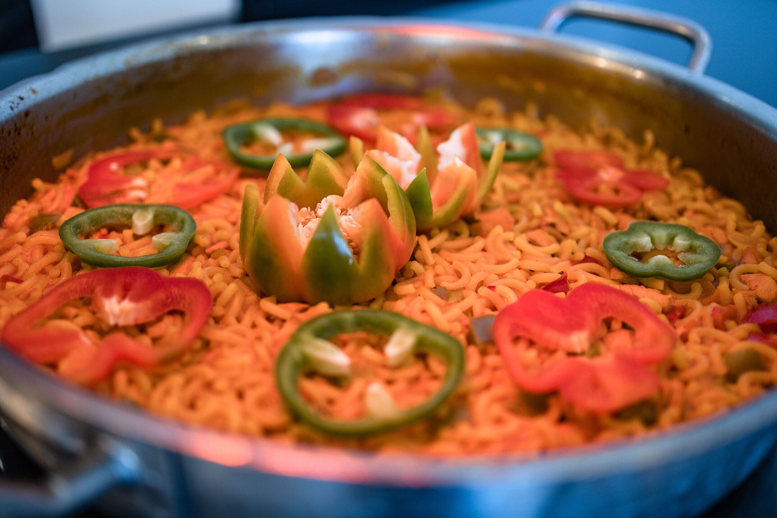 A large metal cooking pot filled with rice and sliced jalapeños.
