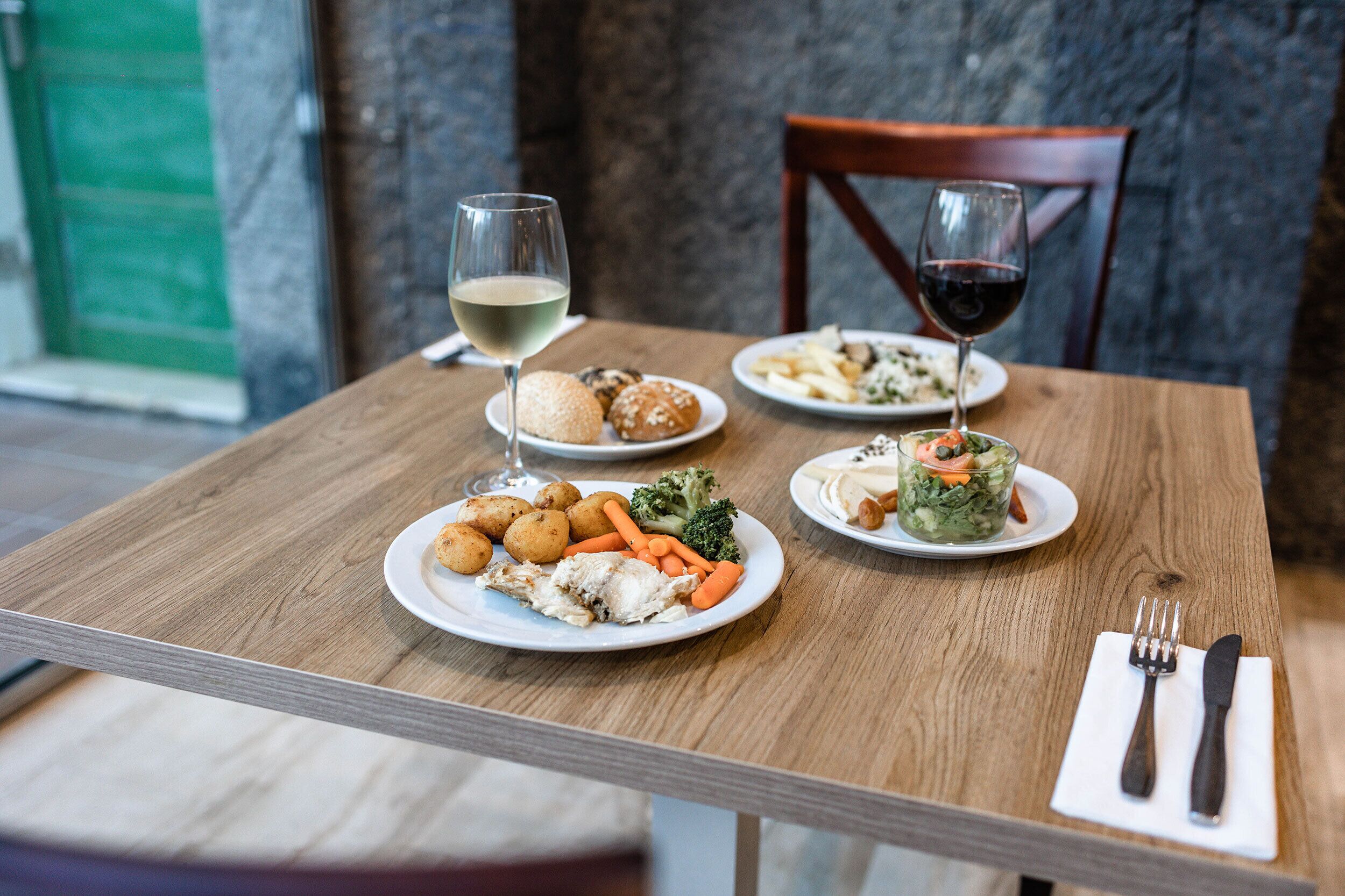 A dining table with plates of food, wine glasses, and cutlery.