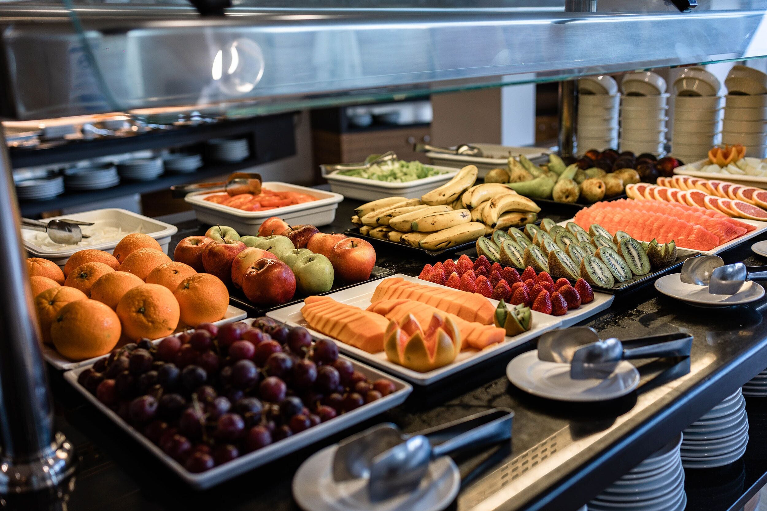 A buffet with various fruits and vegetables, including oranges, apples, grapes, and bananas.