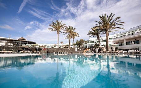 A swimming pool with lounge chairs and palm trees, surrounded by buildings with balconies.