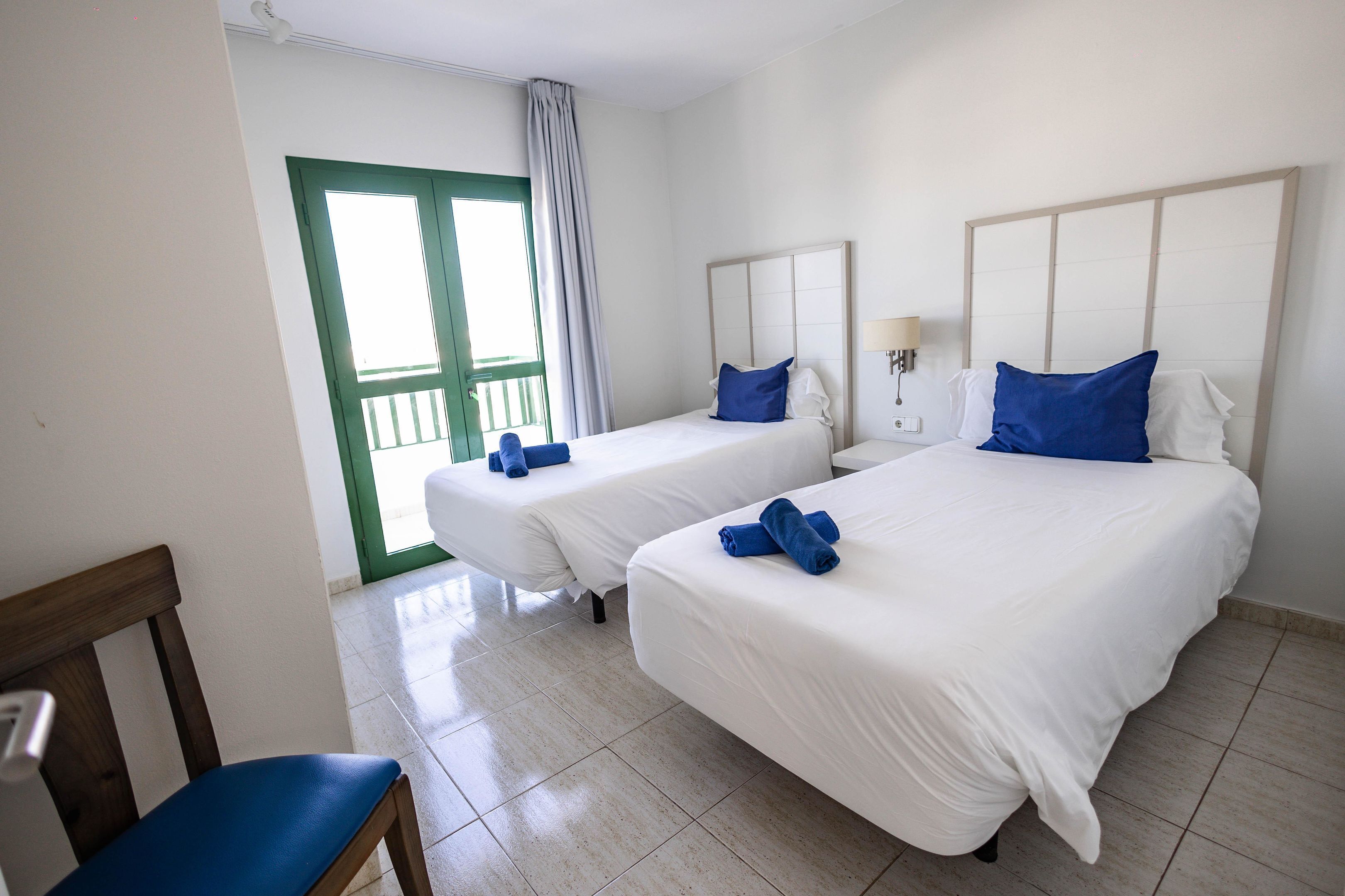 Une chambre d’hôtel avec deux lits, une chaise, une porte dotée d’un cadre vert et une vue à travers la porte.