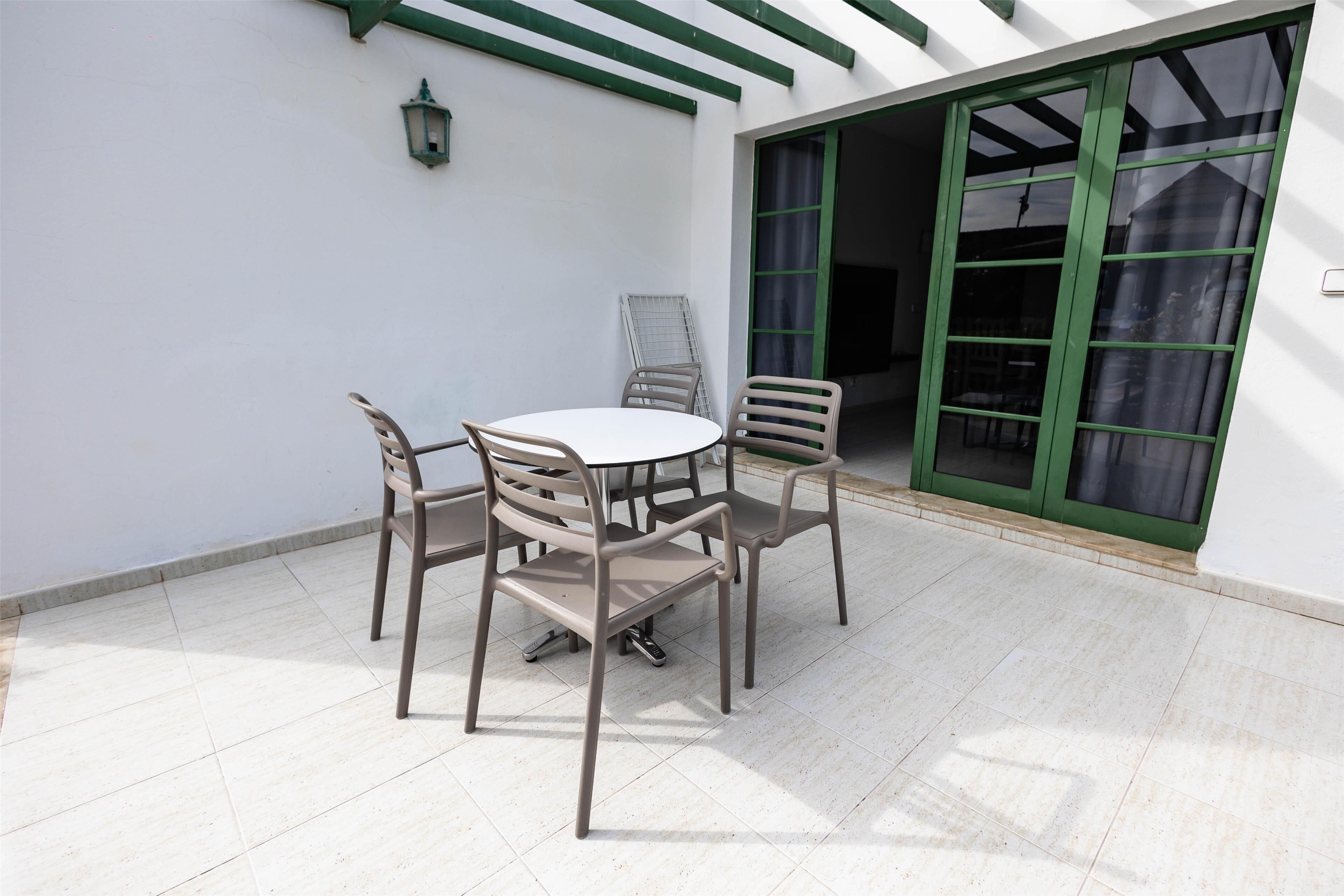 Un patio con un tavolo rotondo e quattro sedie, una porta scorrevole con cornice verde e un muro bianco con un dettaglio verde.