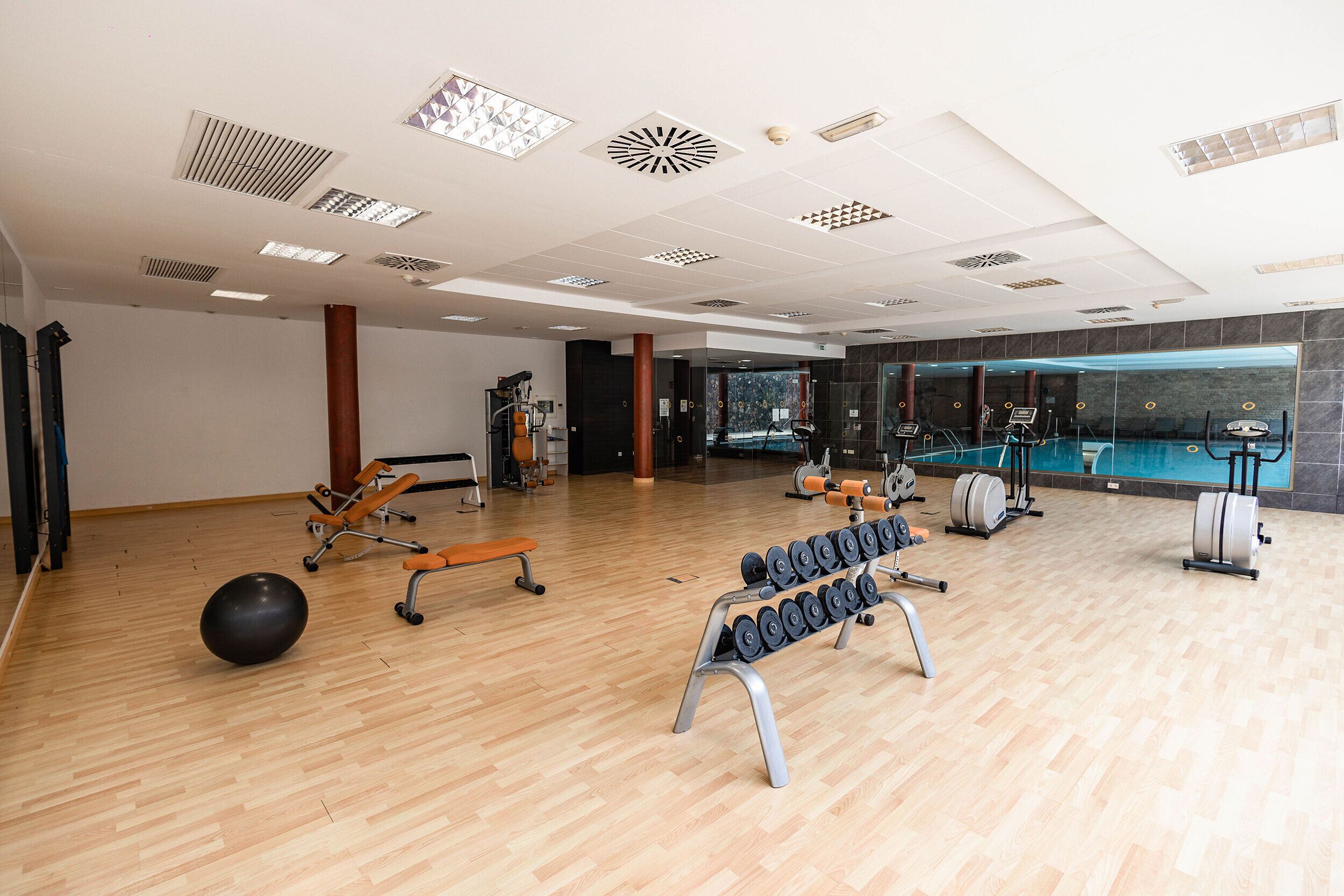 A spacious gym with wooden flooring, exercise equipment, and a large mirror wall.