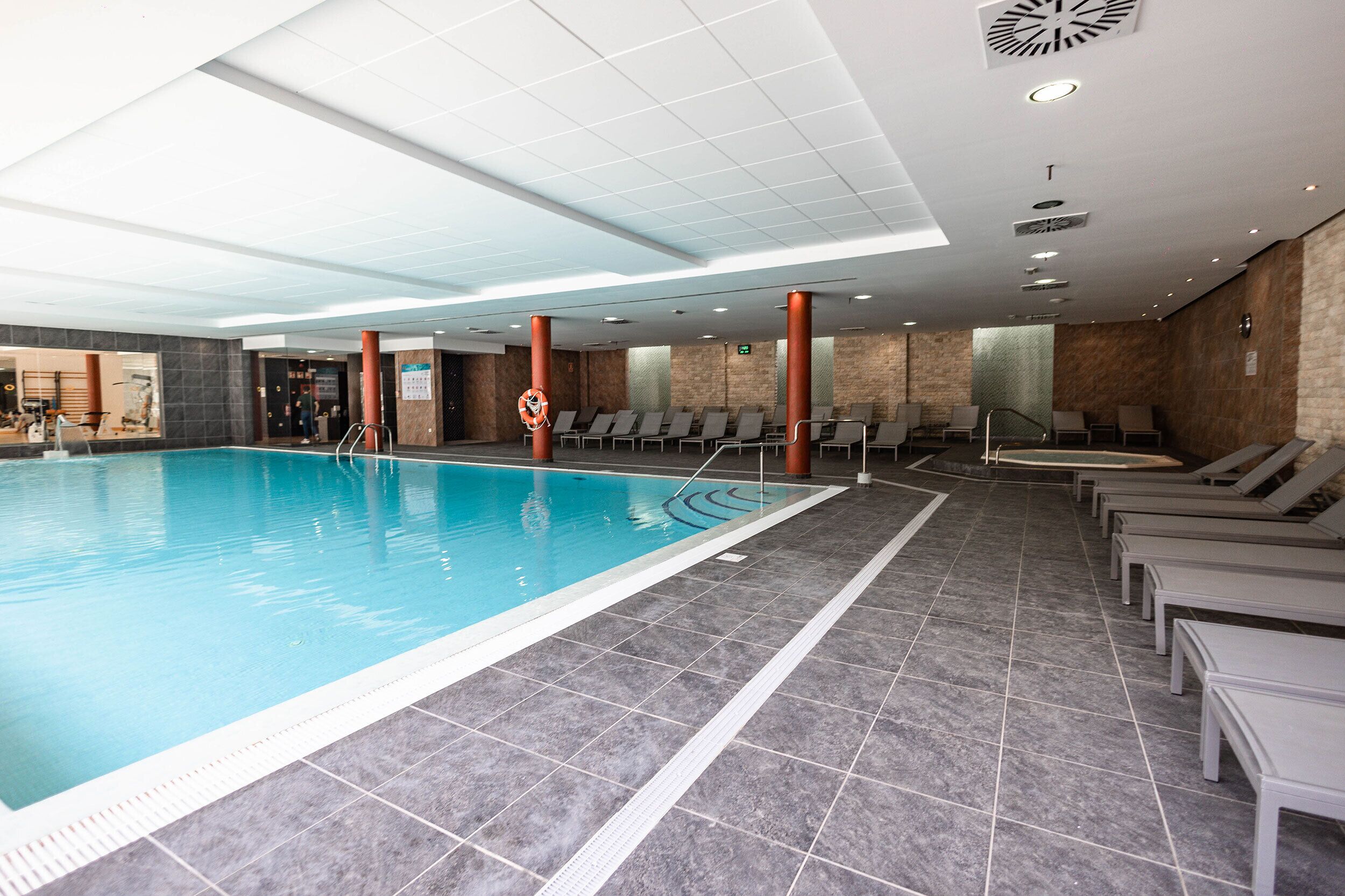 An indoor swimming pool with clear lane markings, adjacent lounge chairs, and a tiled floor.