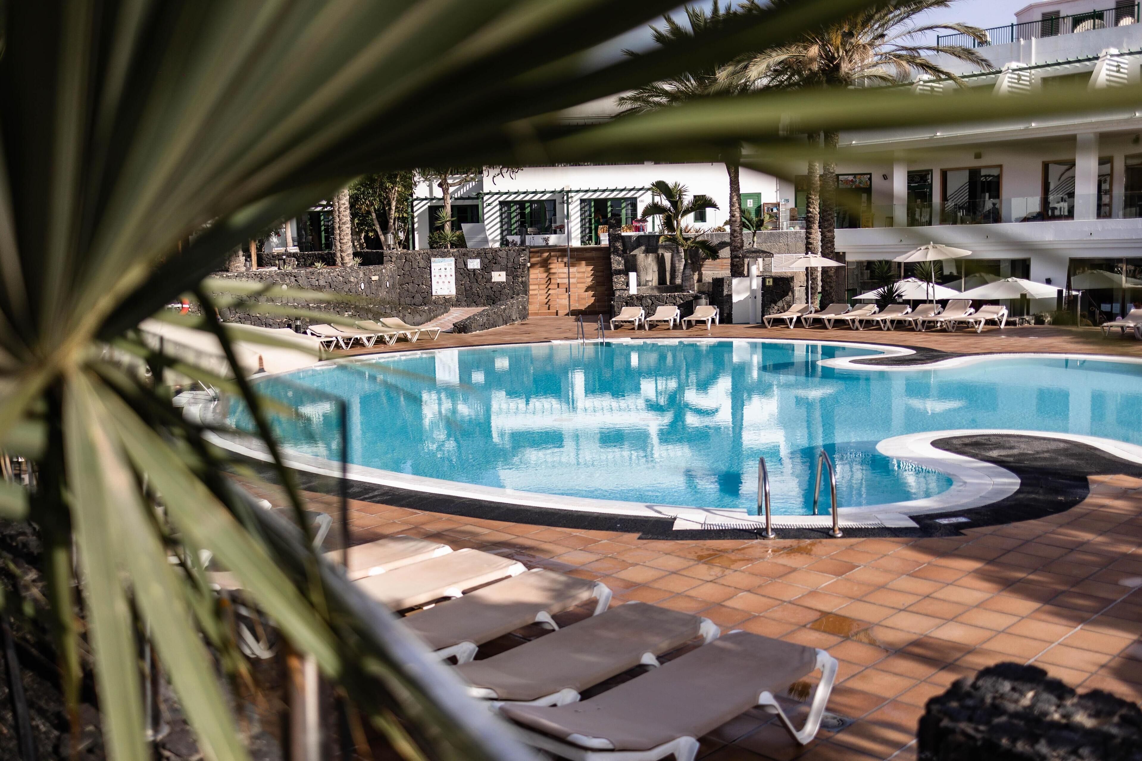 A swimming pool with lounge chairs and umbrellas, surrounded by a building with a tiled patio.
