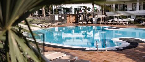A swimming pool with lounge chairs and umbrellas, surrounded by a building with a tiled patio.