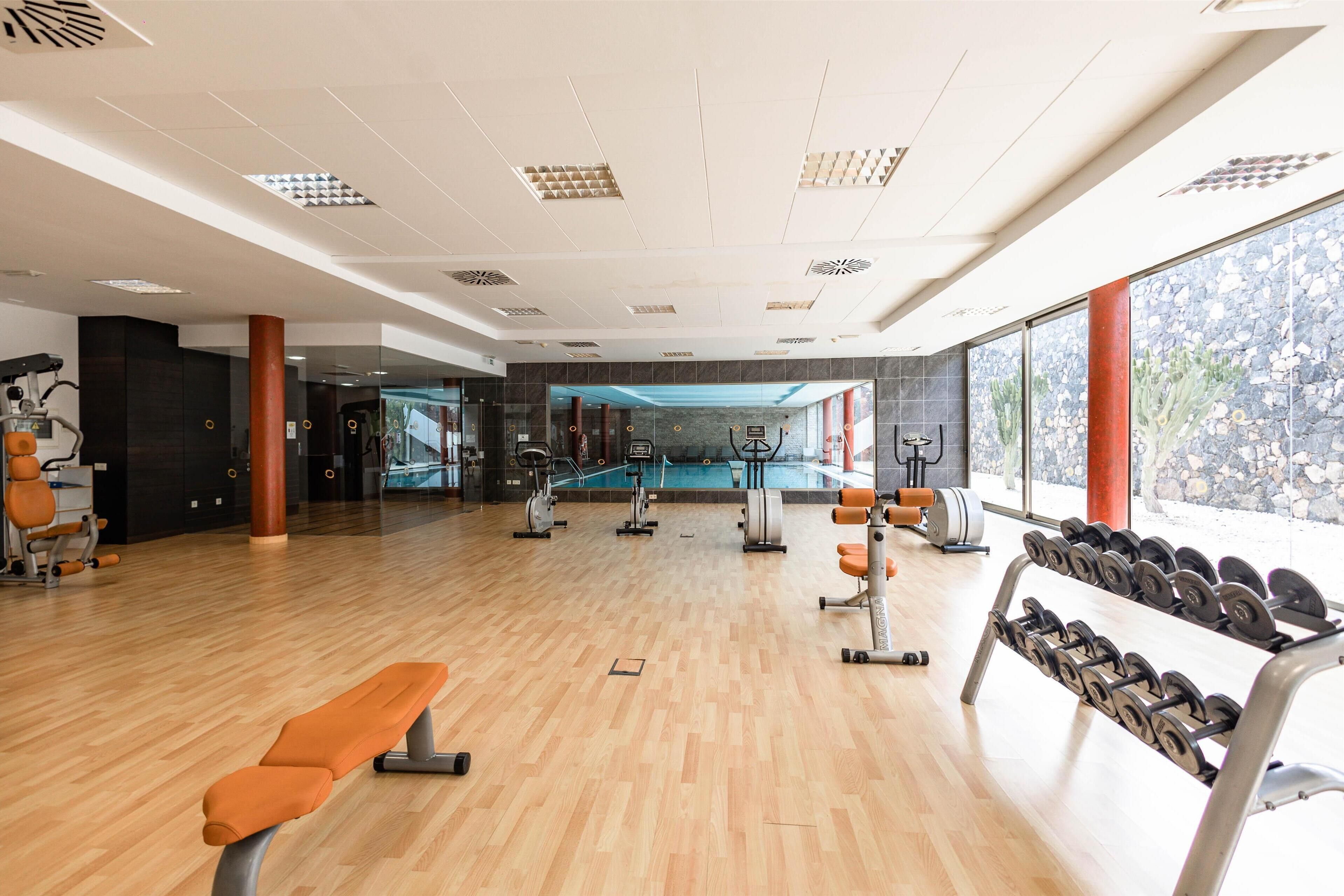 A gym with wooden flooring, exercise equipment, and large windows offering a view of the outdoors.