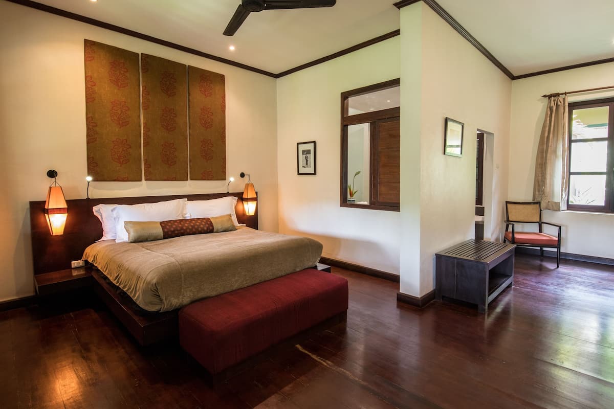 A bedroom with a bed, bedside lamps, a large window, and a wooden floor.