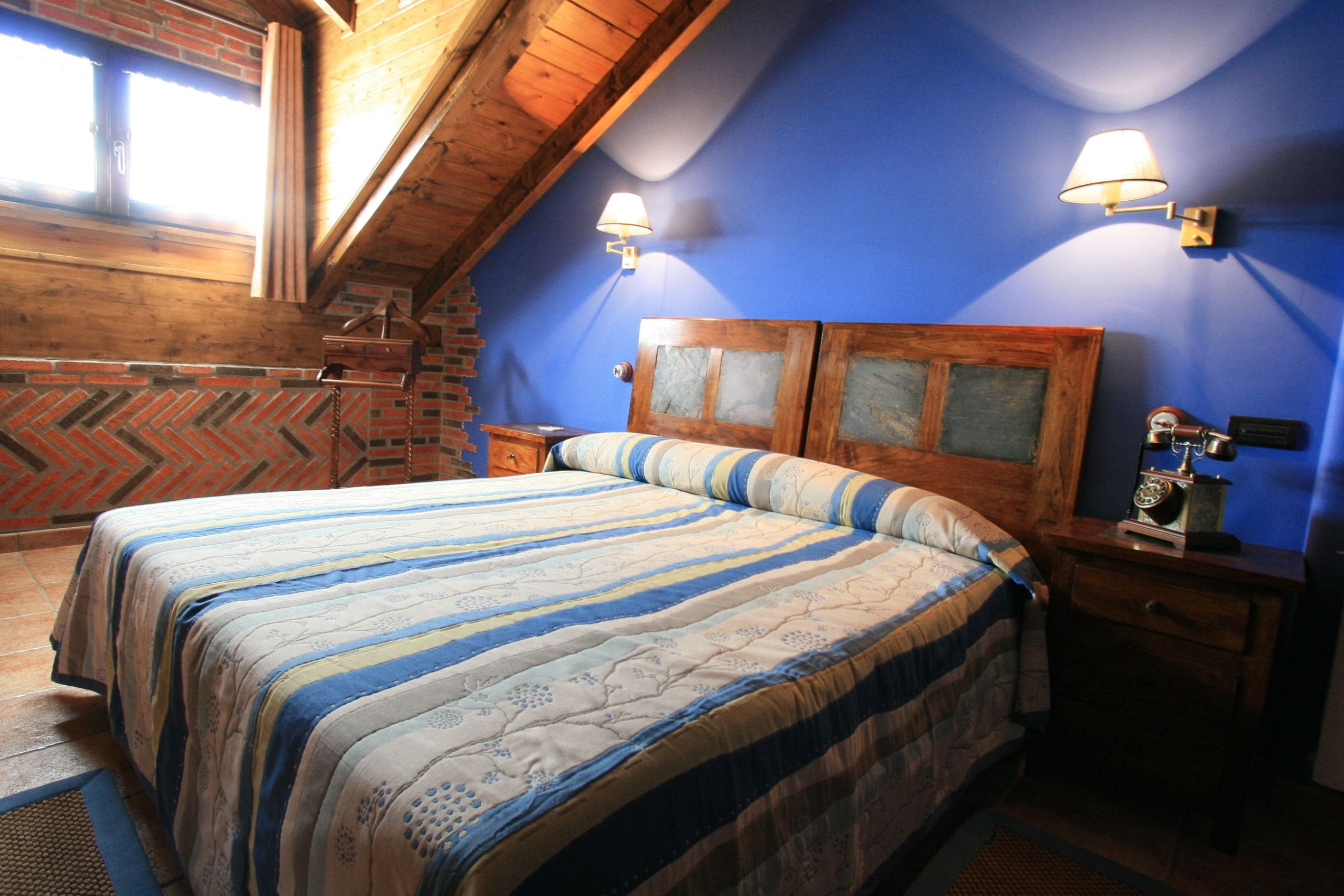 A bedroom with a wooden headboard, a striped bedspread, and two wall-mounted lamps.
