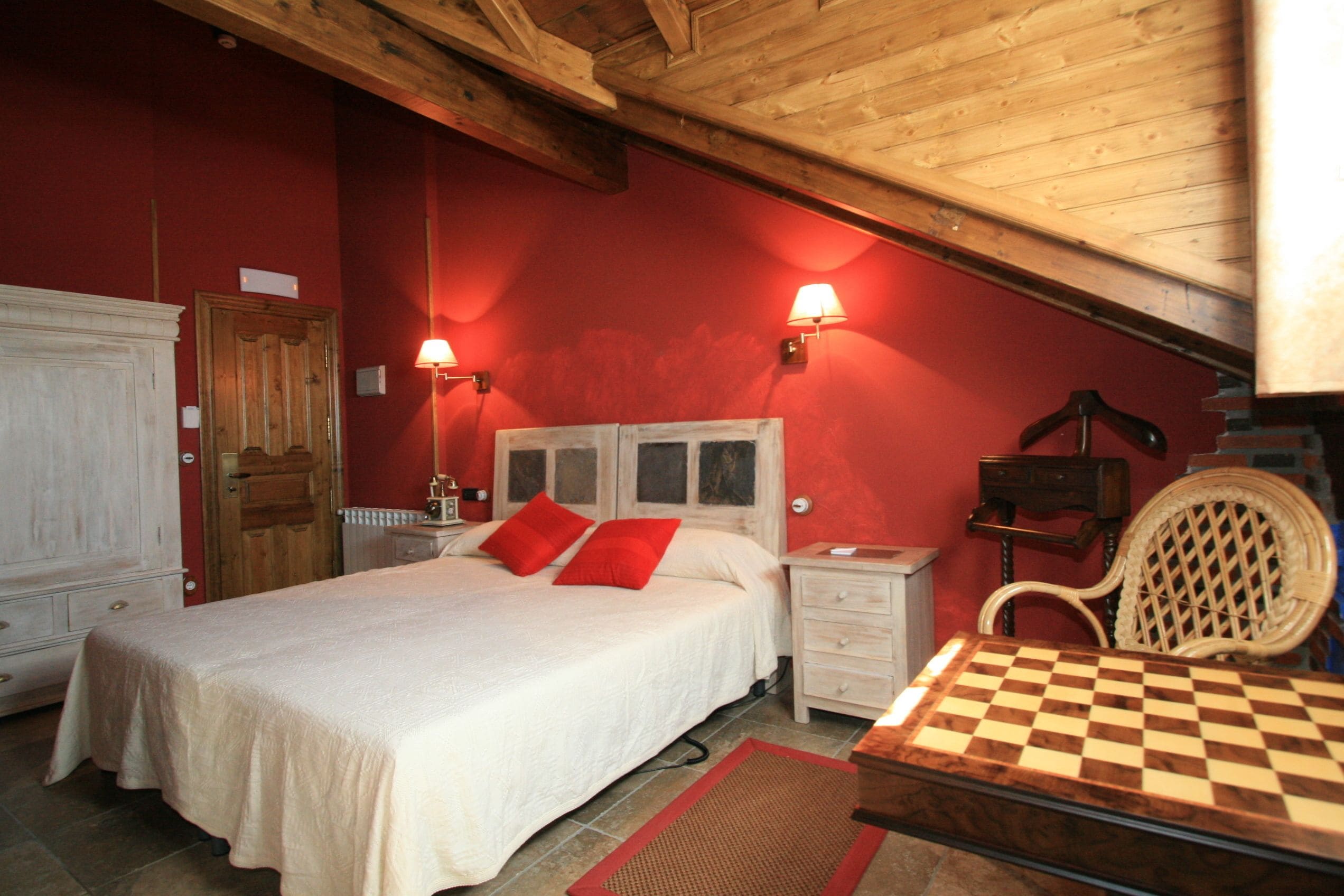 A bedroom with a bed, a nightstand, a chair, and a chessboard.