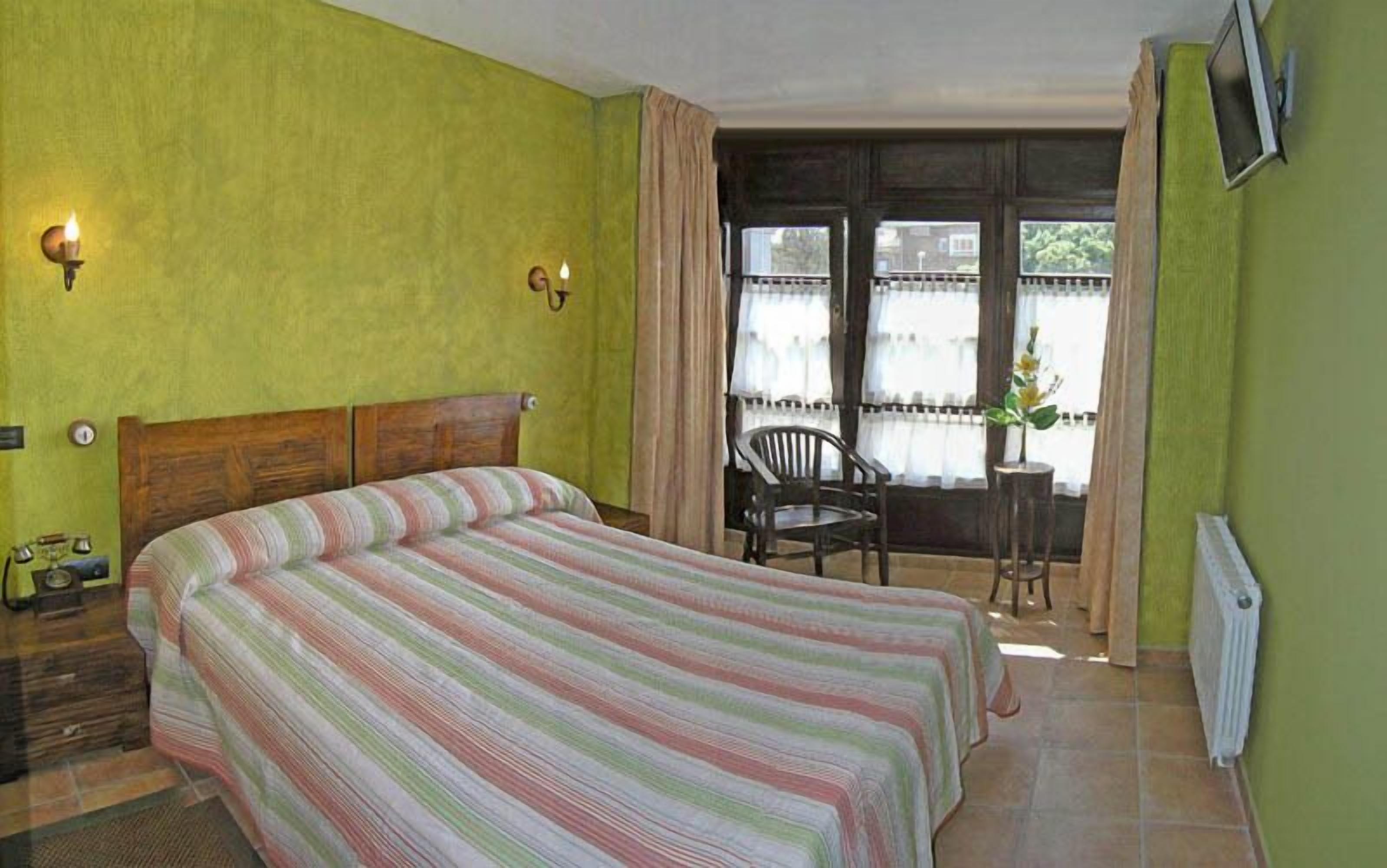 A room with a bed, a chair, a radiator, and a window with curtains.