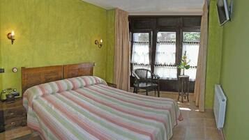A room with a bed, a chair, a radiator, and a window with curtains.