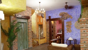 A room with a brick wall, a chandelier, wicker furniture, and a door with decorative ironwork. - Posada Spa Privilegio de Vara (Noja)