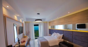 Relax in a spacious room with a large bed, flat-screen TV, and balcony offering a view of the surrounding landscape.