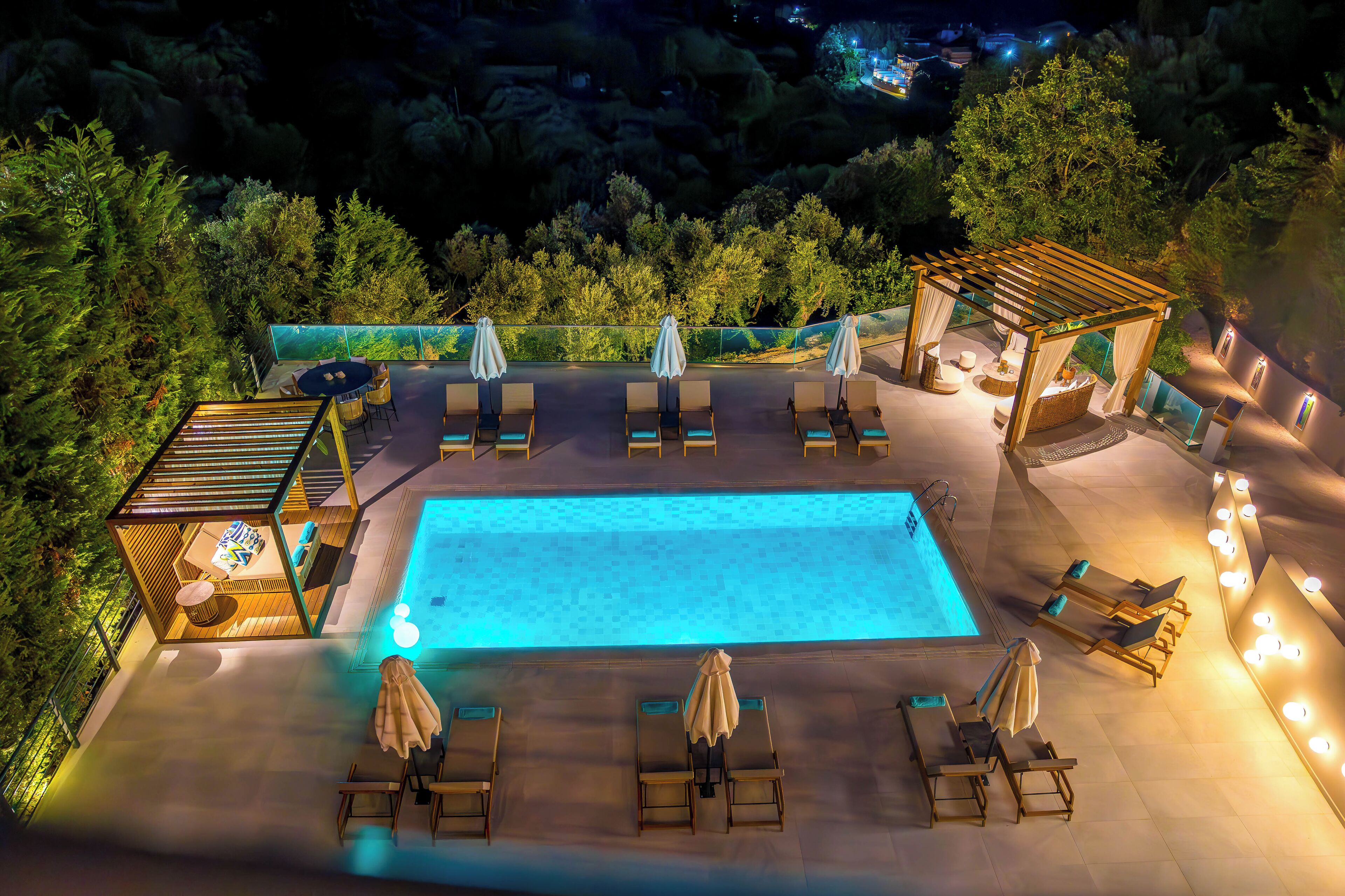 Un área de piscina en la azotea con sillones de descanso y sombrillas, rodeada de vegetación.