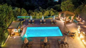 Un área de piscina en la azotea con sillones de descanso y sombrillas, rodeada de vegetación.