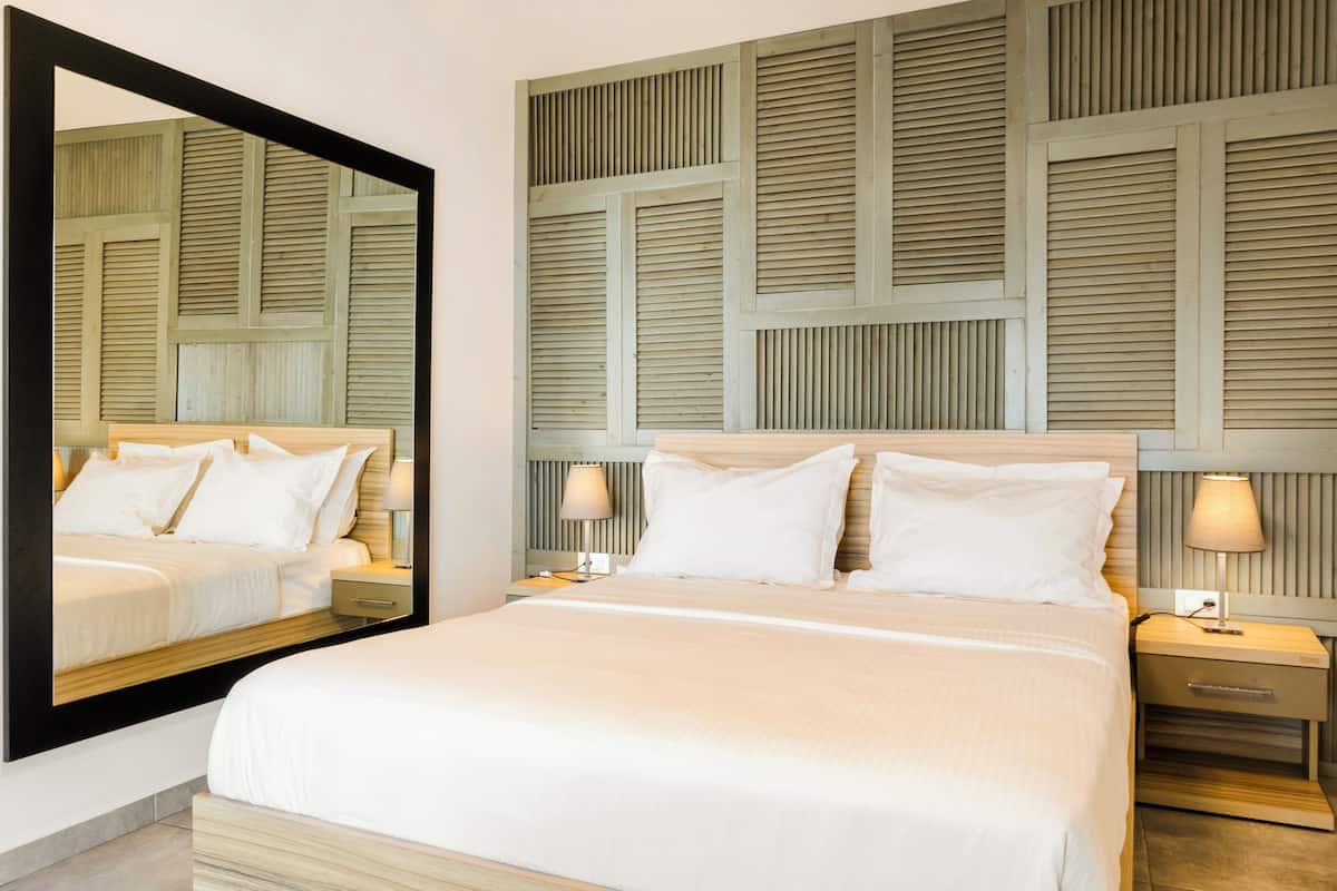 A hotel room with a large bed, a nightstand with a lamp, and a mirror reflecting the room.