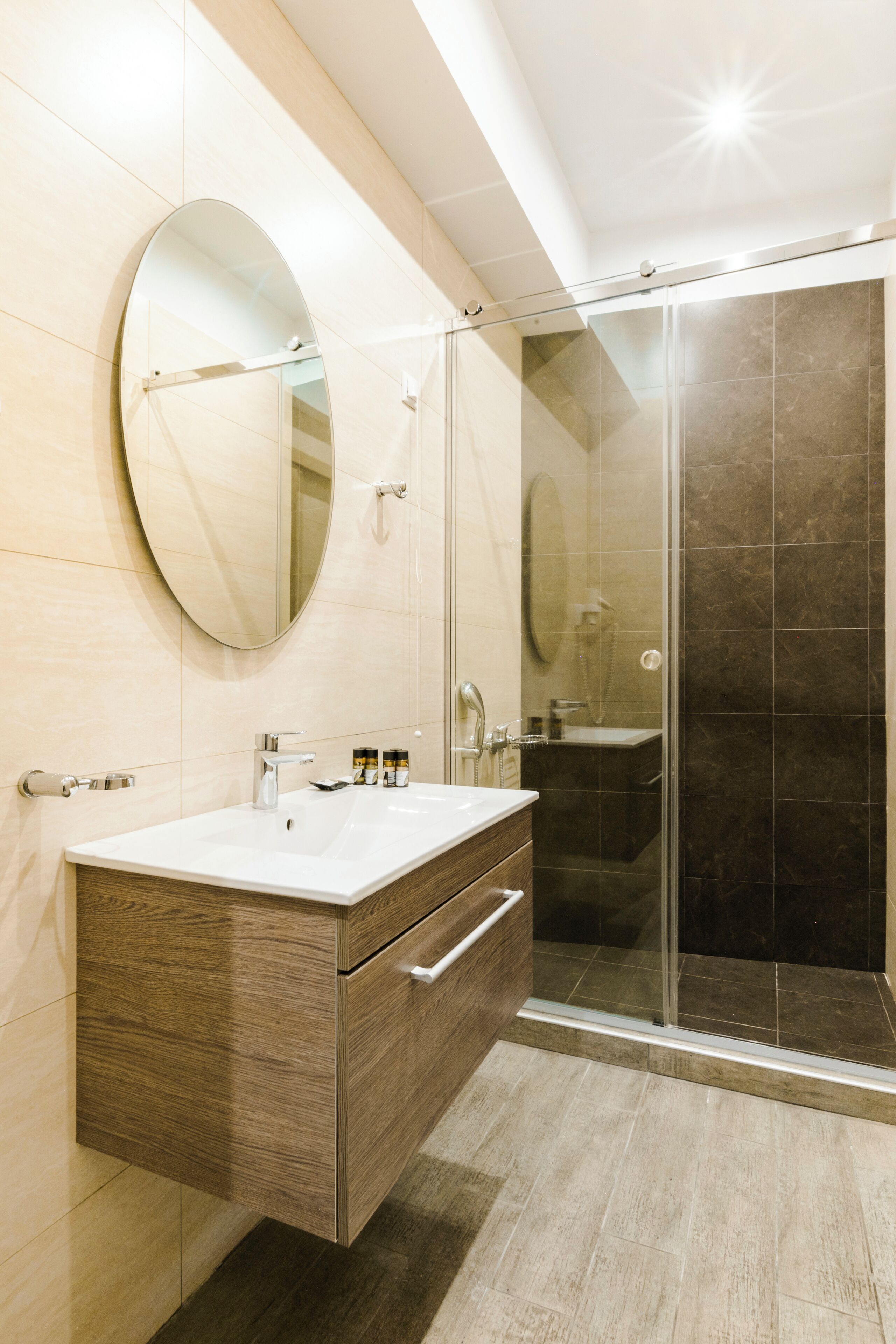 A modern bathroom with a wooden vanity, a large mirror, and a glass-enclosed shower.