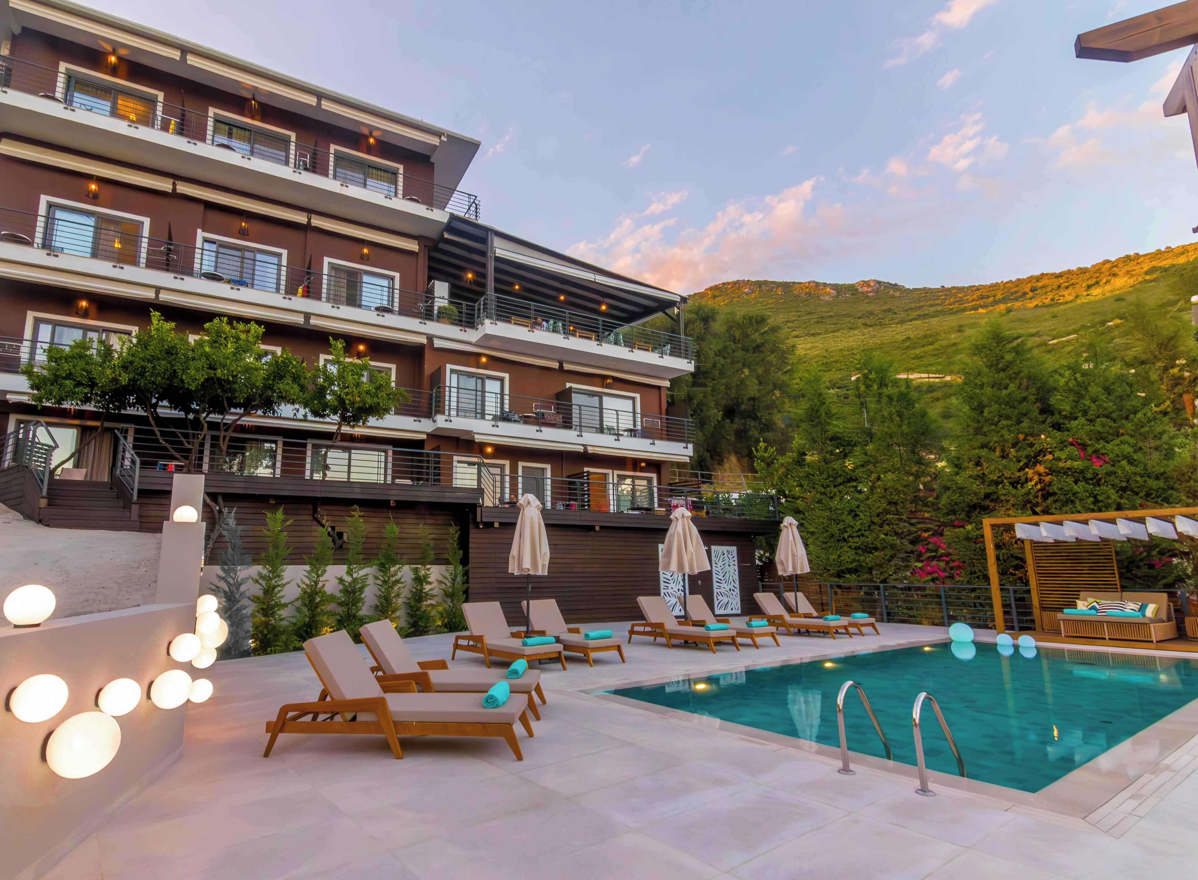 Un hotel con zona de piscina, varios balcones y vistas a una colina.