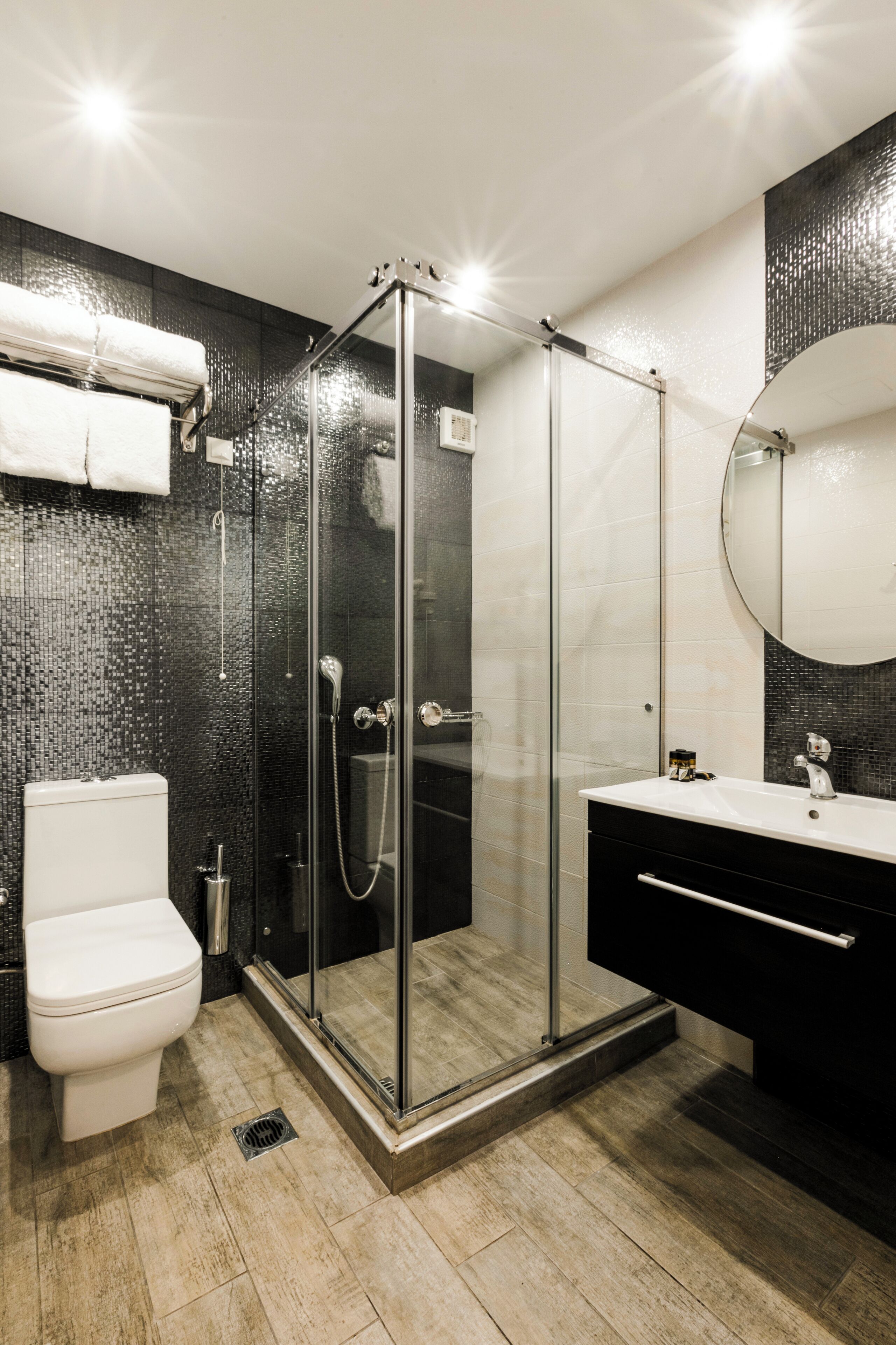 A modern bathroom with a glass-enclosed shower, a white toilet, a black vanity with a mirror, and a tiled floor.