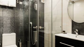 A modern bathroom with a glass-enclosed shower, a white toilet, a black vanity with a mirror, and a tiled floor.