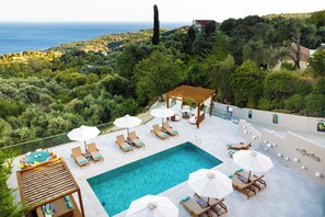 Relax by the pool surrounded by lush greenery and a distant sea view.